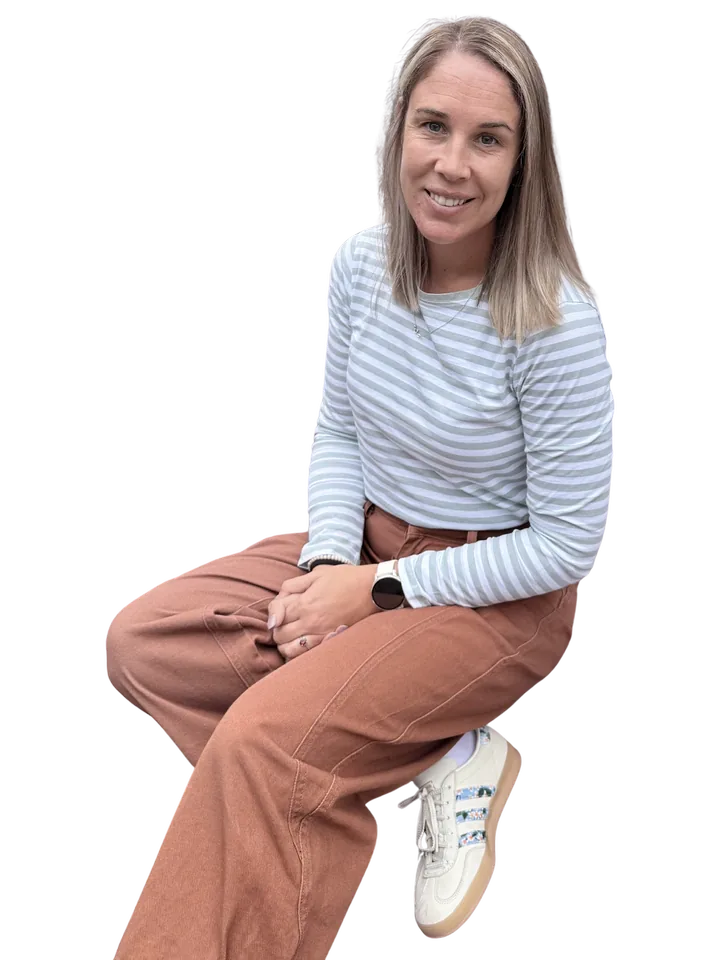 Tarryn, seated and smiling, in a soft striped top and rust-coloured trousers.