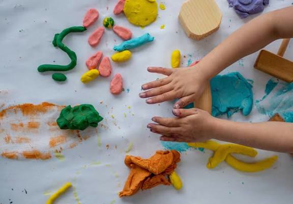 A child's hands pressing into brightly coloured modelling clay spread across a table.