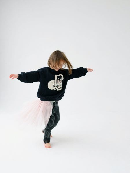 A child dancing barefoot in a pale tutu, arms stretched wide.