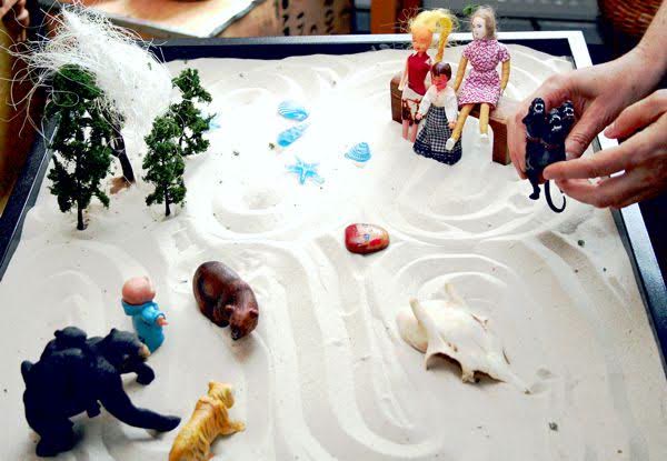 A sand tray scene with miniature trees, shells, animals and a family of small figures.